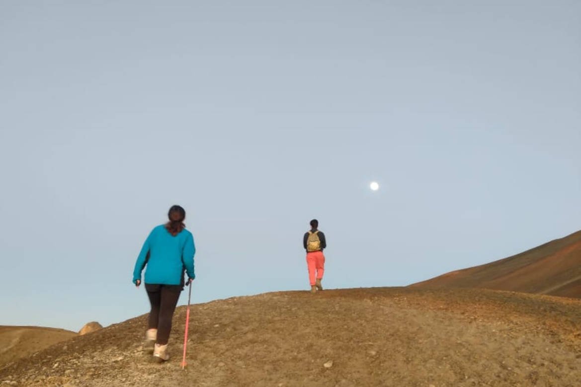 Two hikers with poles crossing volcanic scree at dusk
