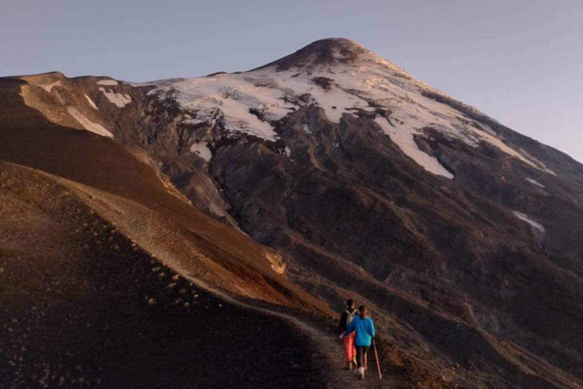 Two hikers on a volcanic scree trail below Osorno Volcano at sunset
