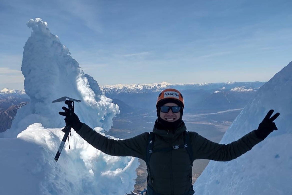 Persona levanta un piolet junto a una formación de hielo, con un valle de fondo