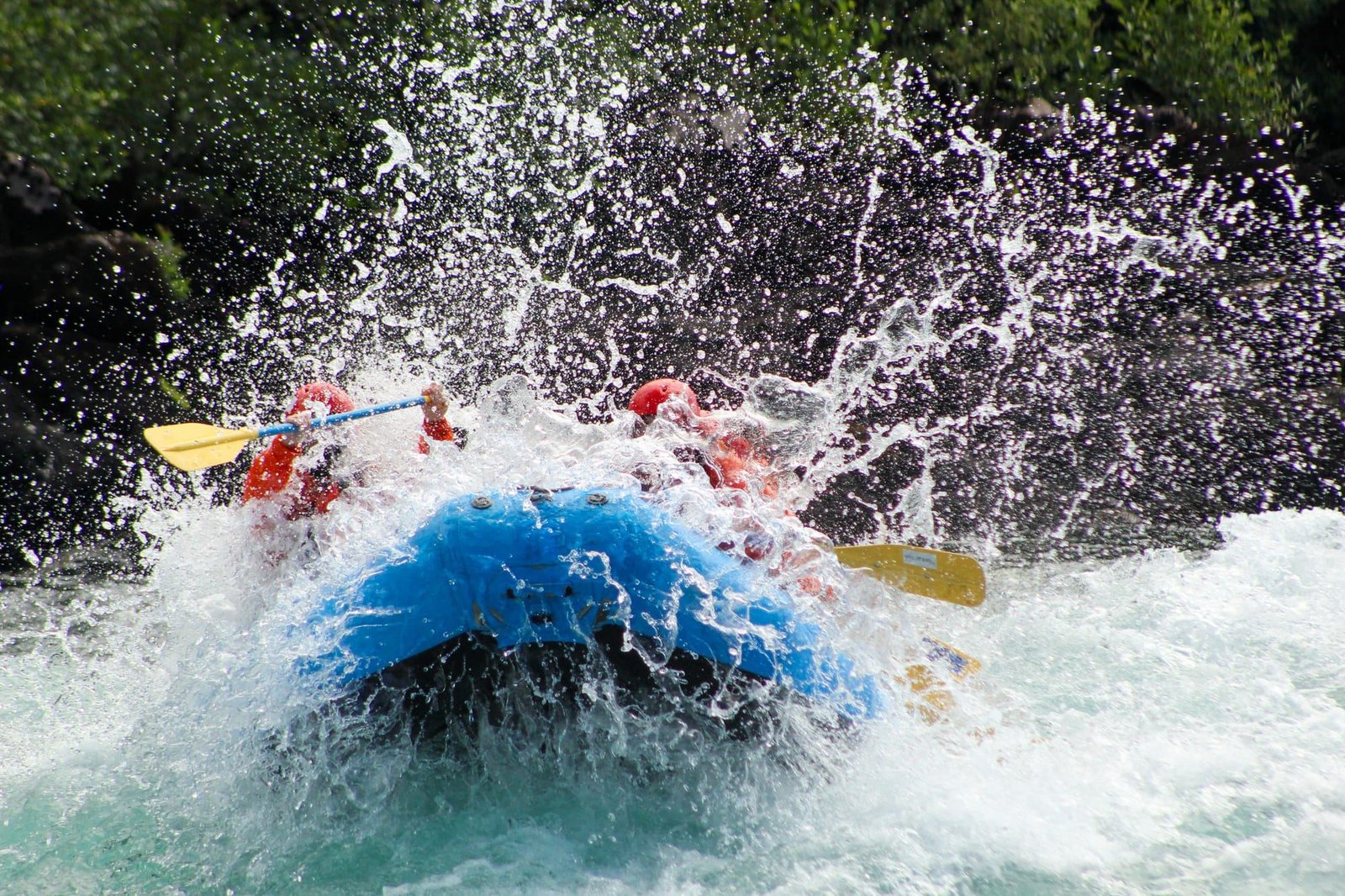 A blue raft punches through a wave that sprays the whole group
