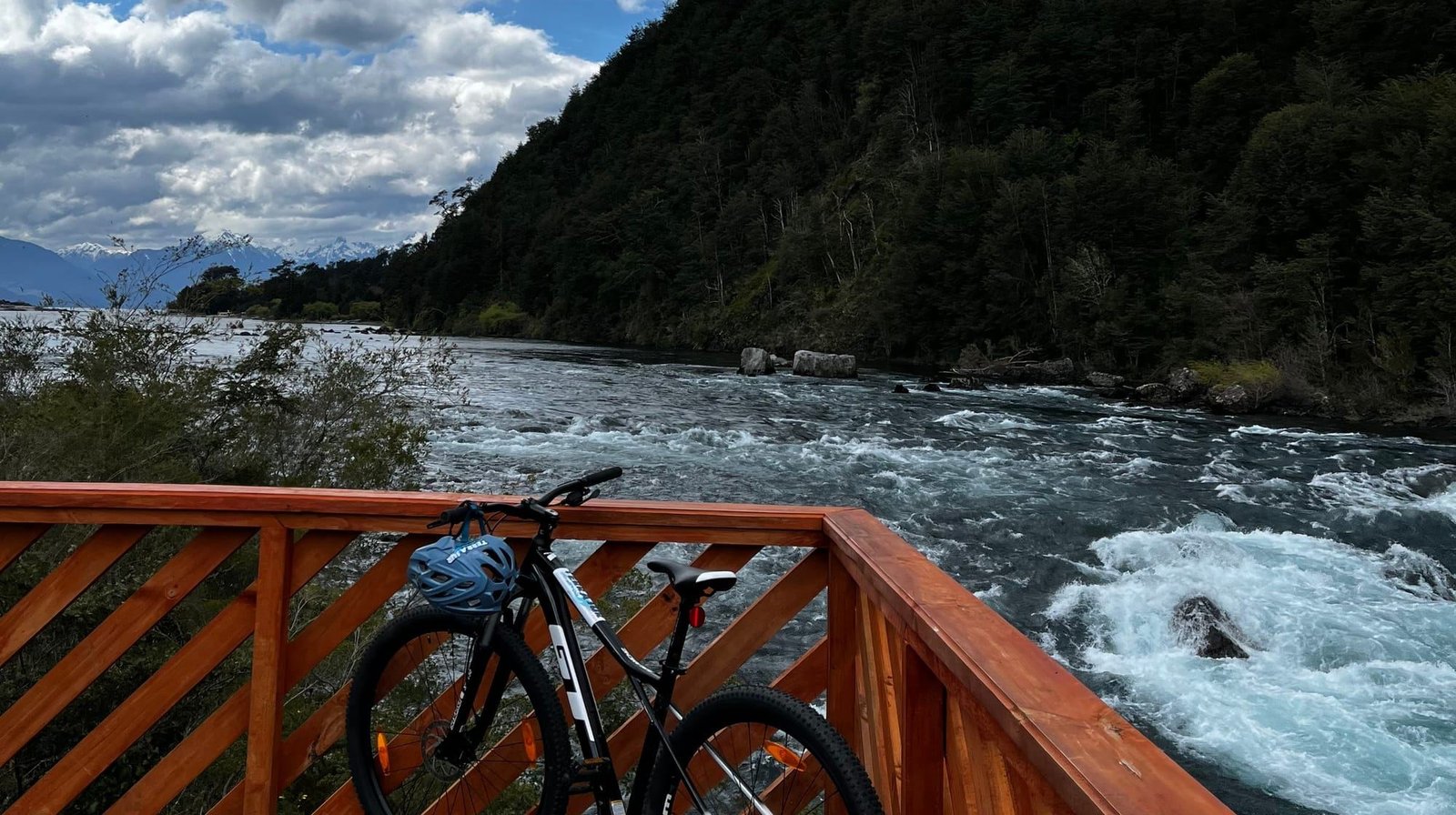 Bicicleta de montaña apoyada en un mirador de madera sobre un río de aguas blancas