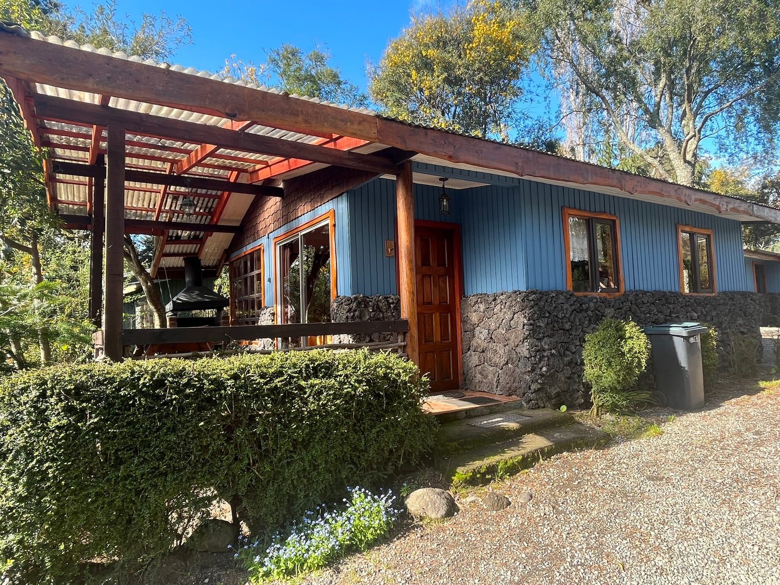 A blue wooden cabin with a stone base and a covered terrace