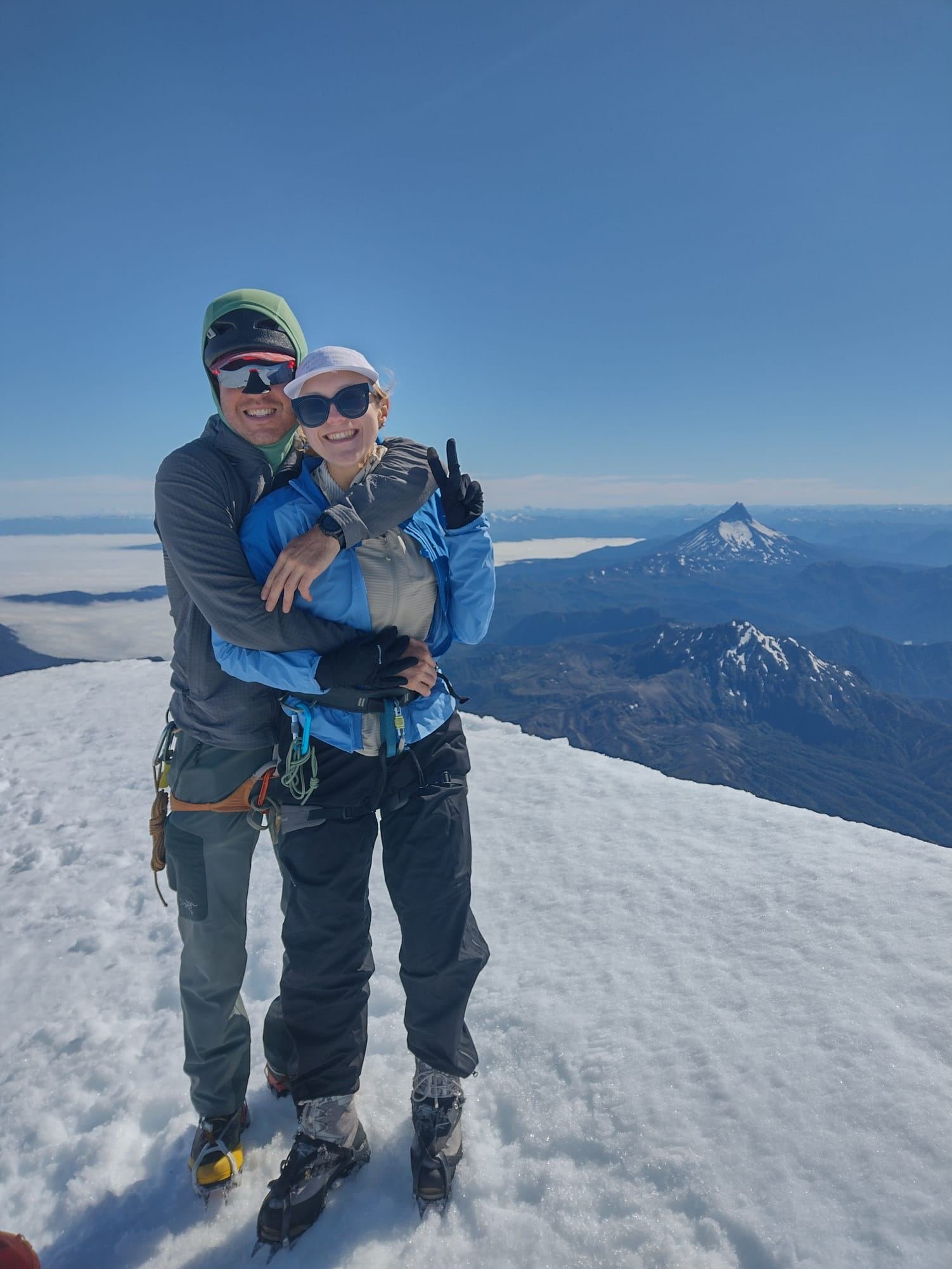 Two people on the snowy summit of Osorno Volcano, with another volcano behind