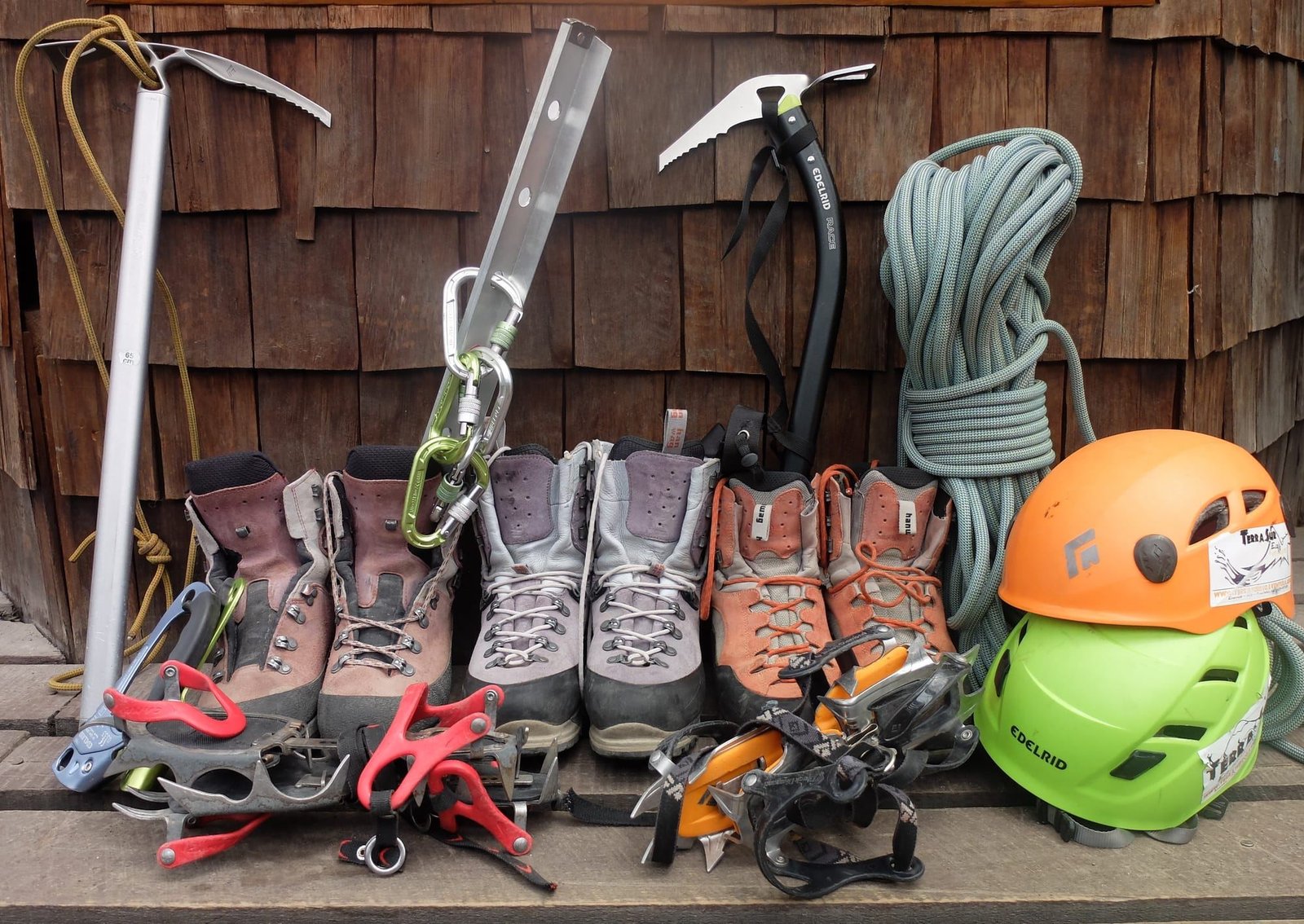 Botas, crampones, piolets, cuerda y cascos de montaña ordenados contra un muro de tejuelas