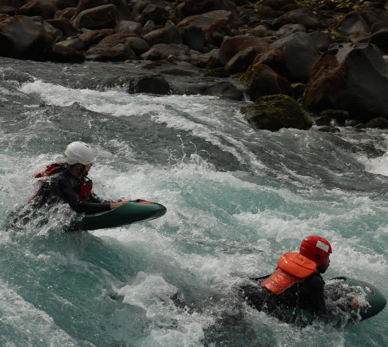 Dos personas en tablas de hidrospeed entre aguas blancas y rocas