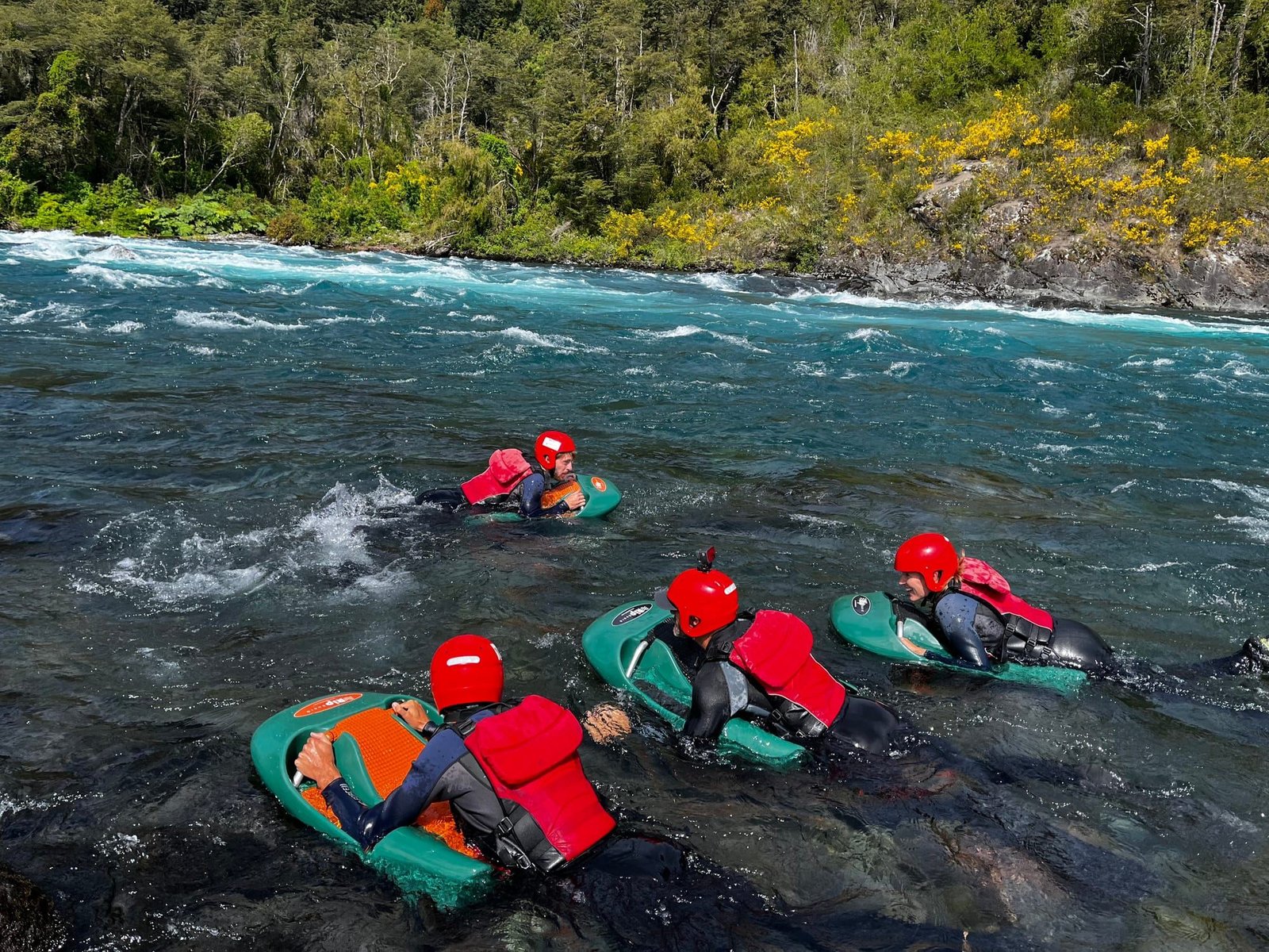 Three people in red helmets on hydrospeed boards on the Petrohue River