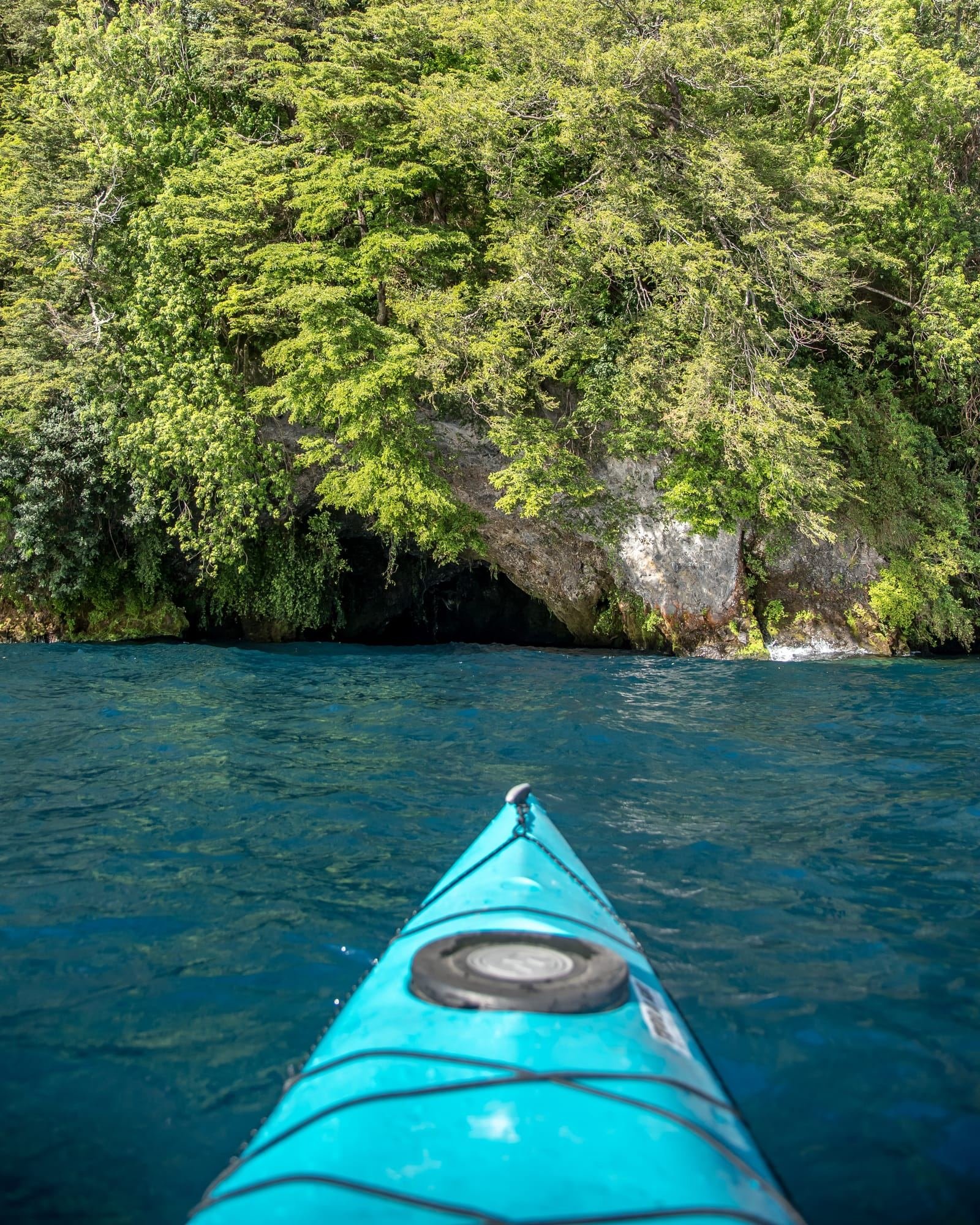 Proa de un kayak turquesa frente a una caverna de roca en el Lago Llanquihue