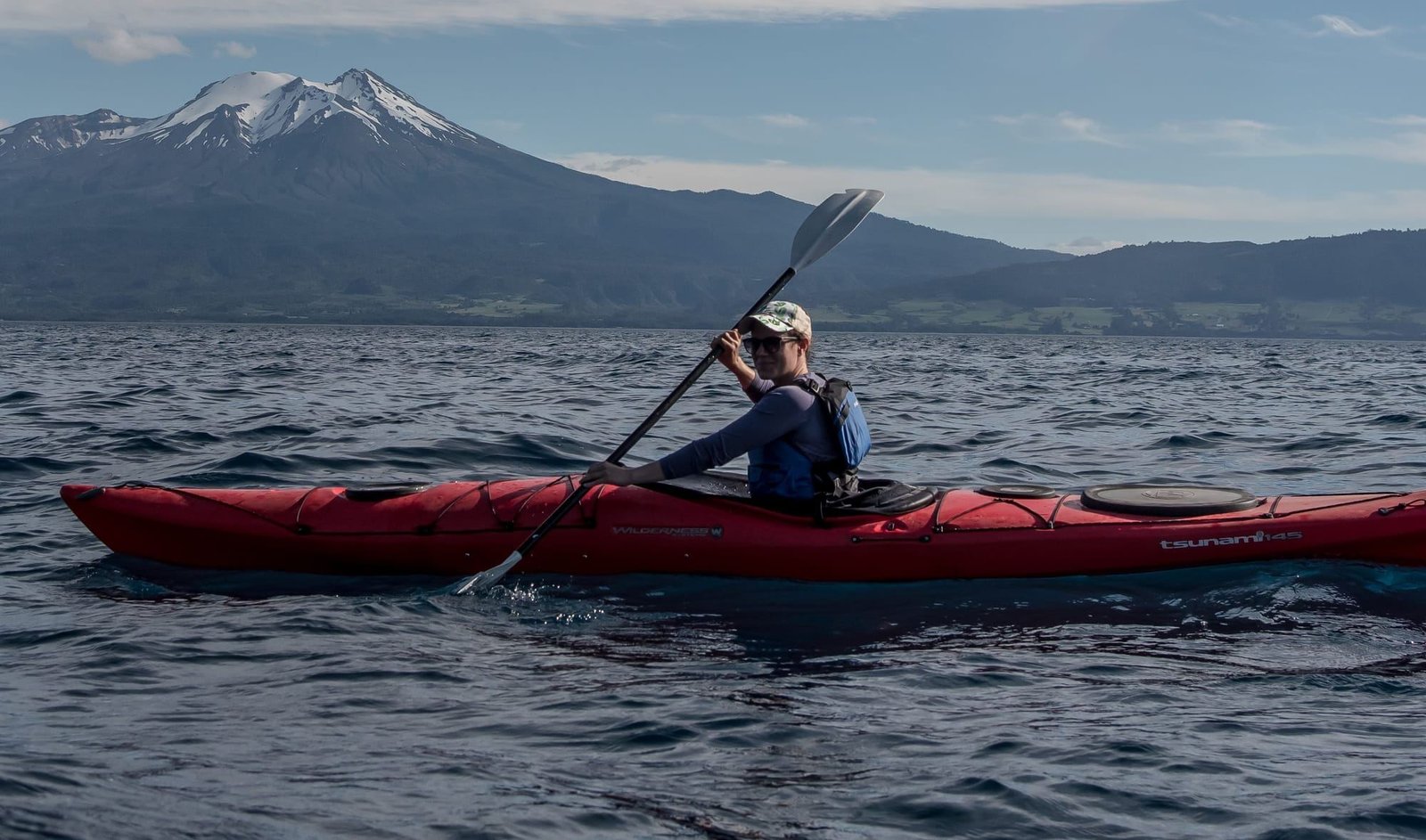 Persona rema un kayak de mar rojo en el Lago Llanquihue, con un volcán nevado al fondo