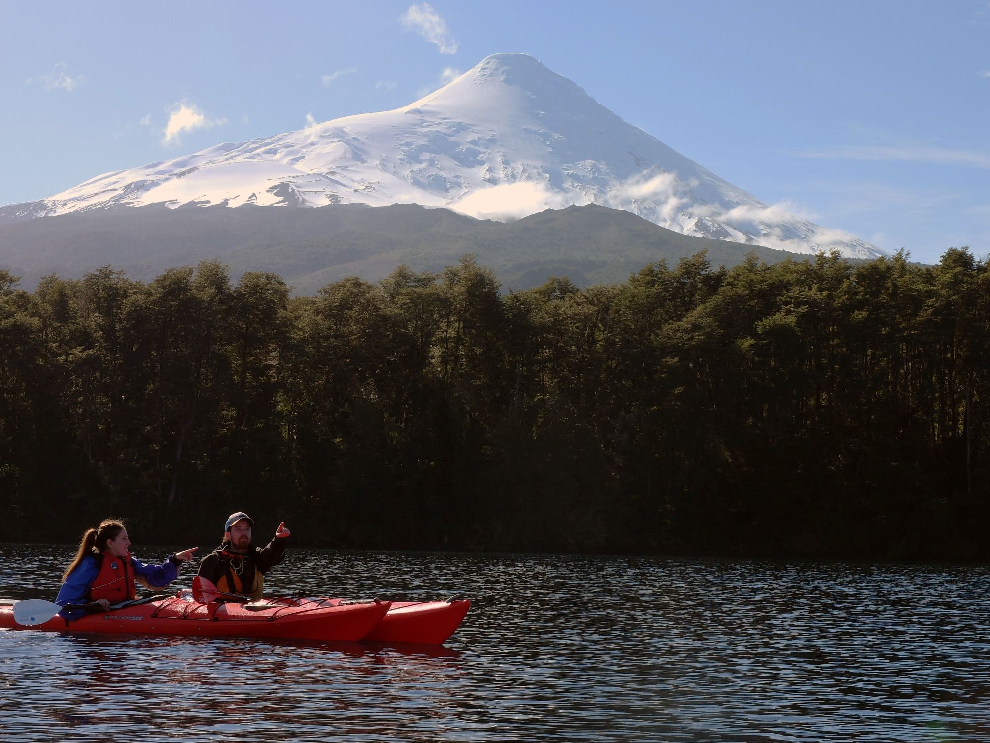 A double kayak on Lake Llanquihue in front of the Vicente Pérez Rosales forest, with snow-capped Osorno Volcano