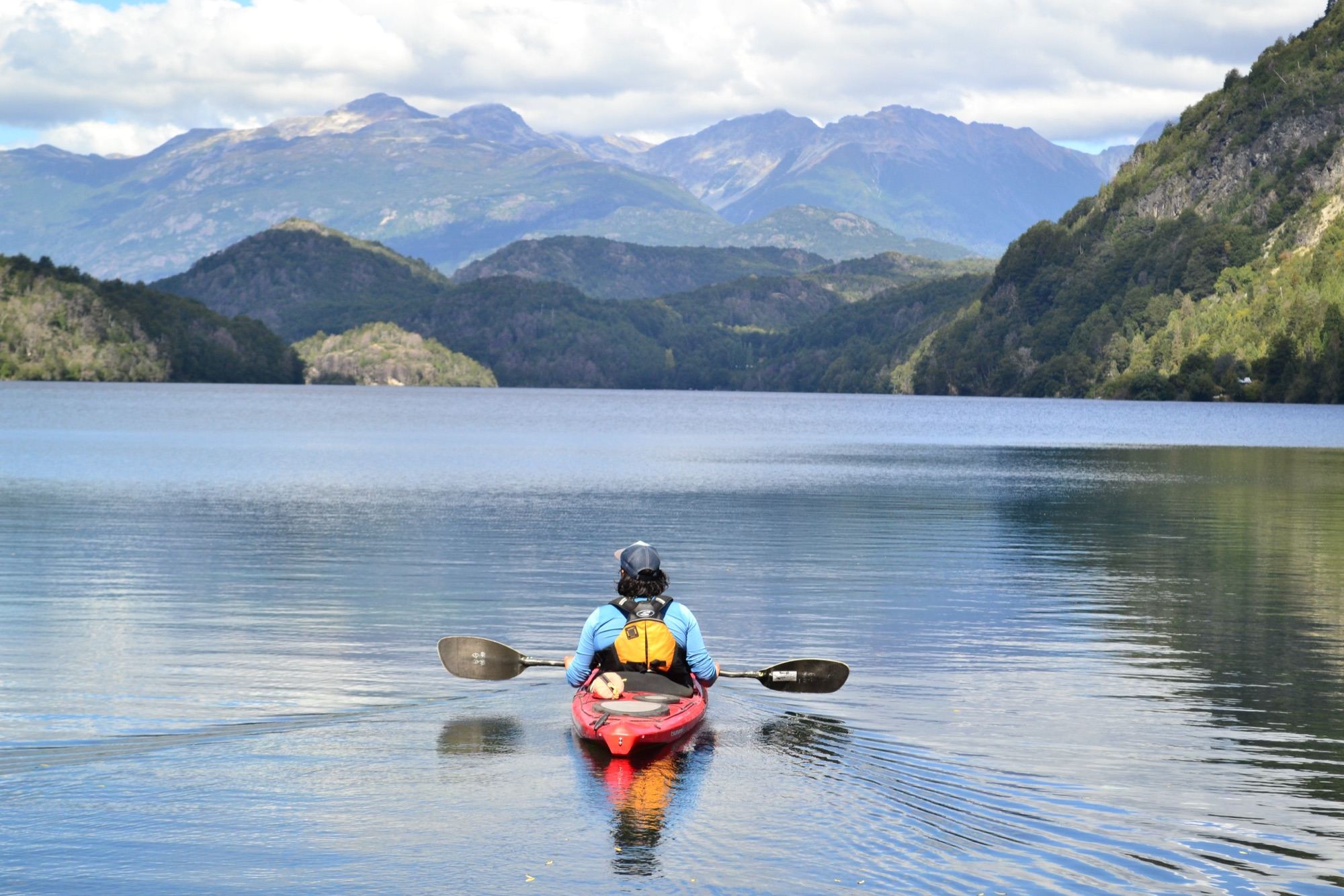 A kayaker on Lake Las Rocas, with forested hills and mountains behind