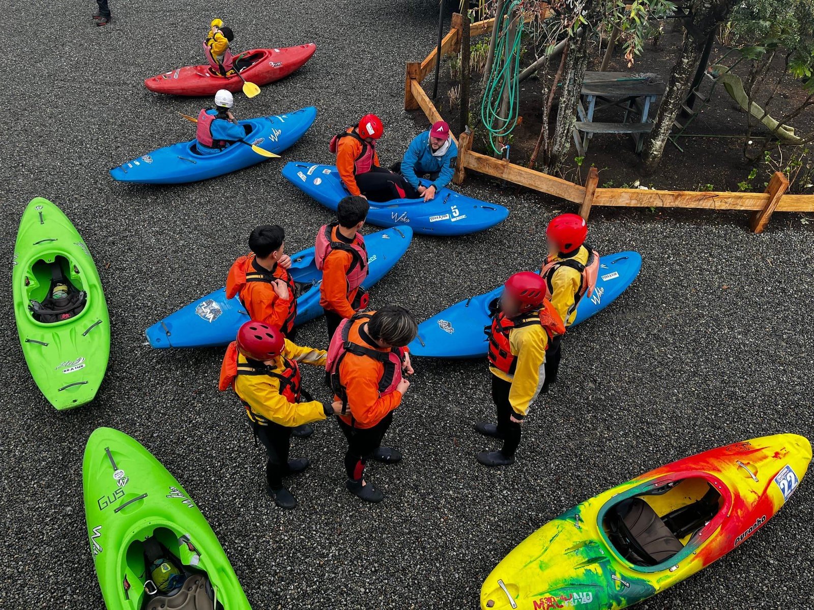 A group in helmets and life jackets beside river kayaks, seen from above