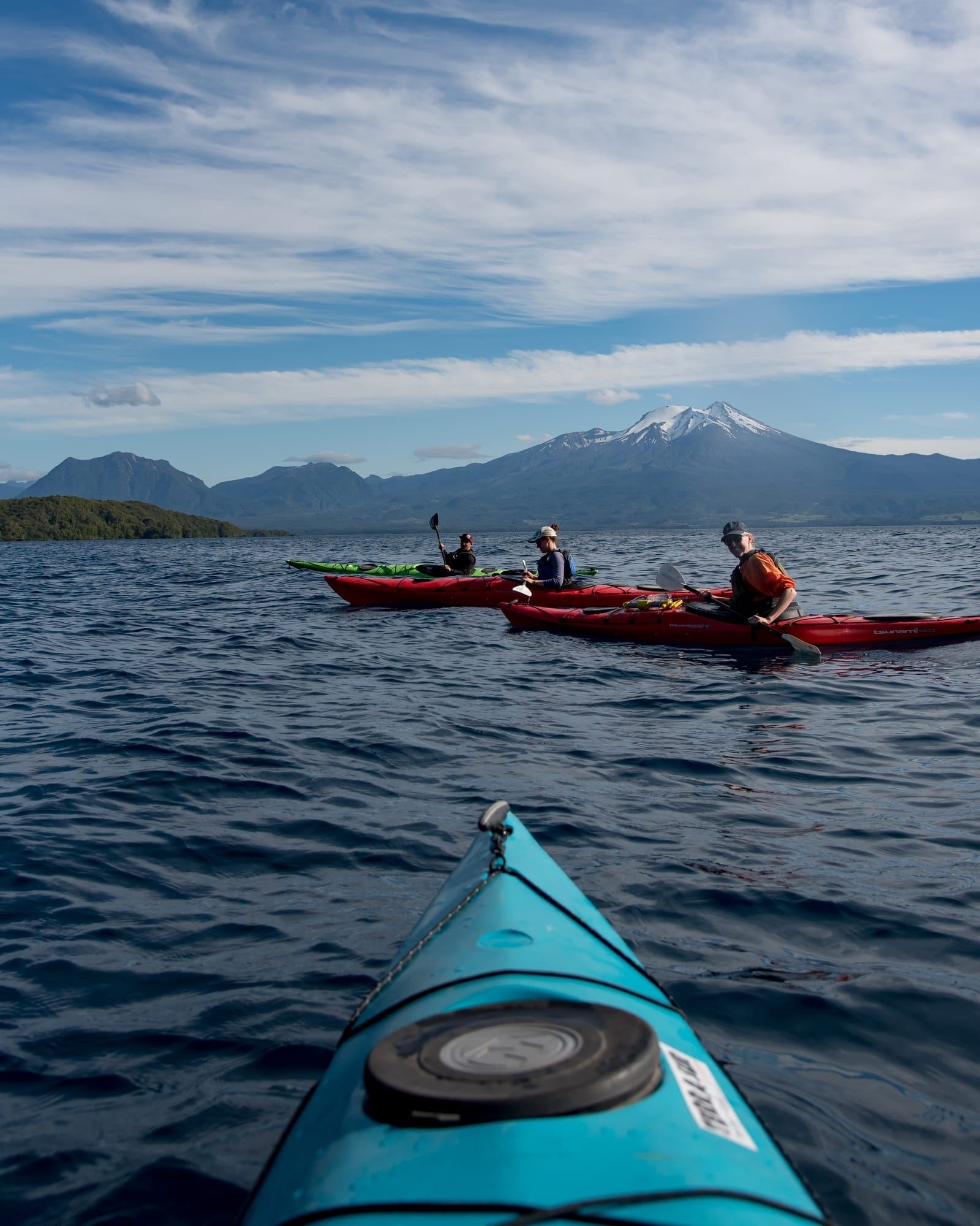 Grupo en kayaks de travesía rojos visto desde la proa de un kayak turquesa