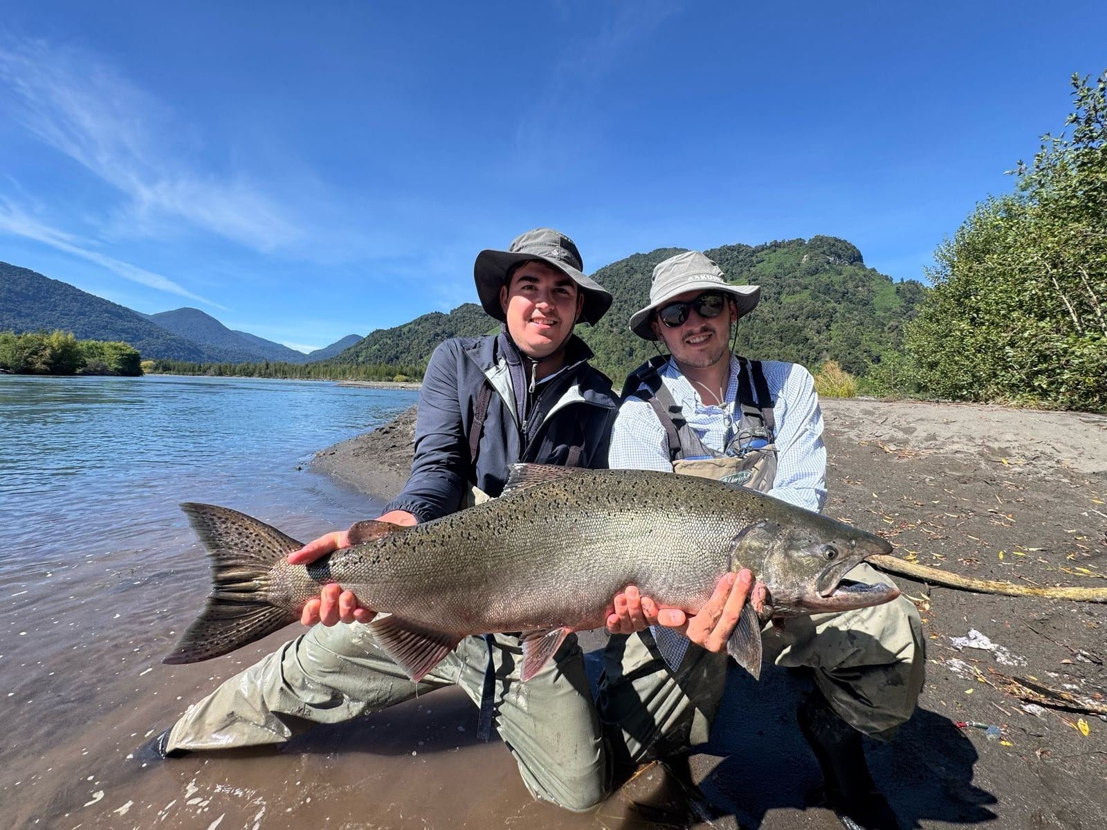 Dos pescadores sostienen un salmón en la orilla del río
