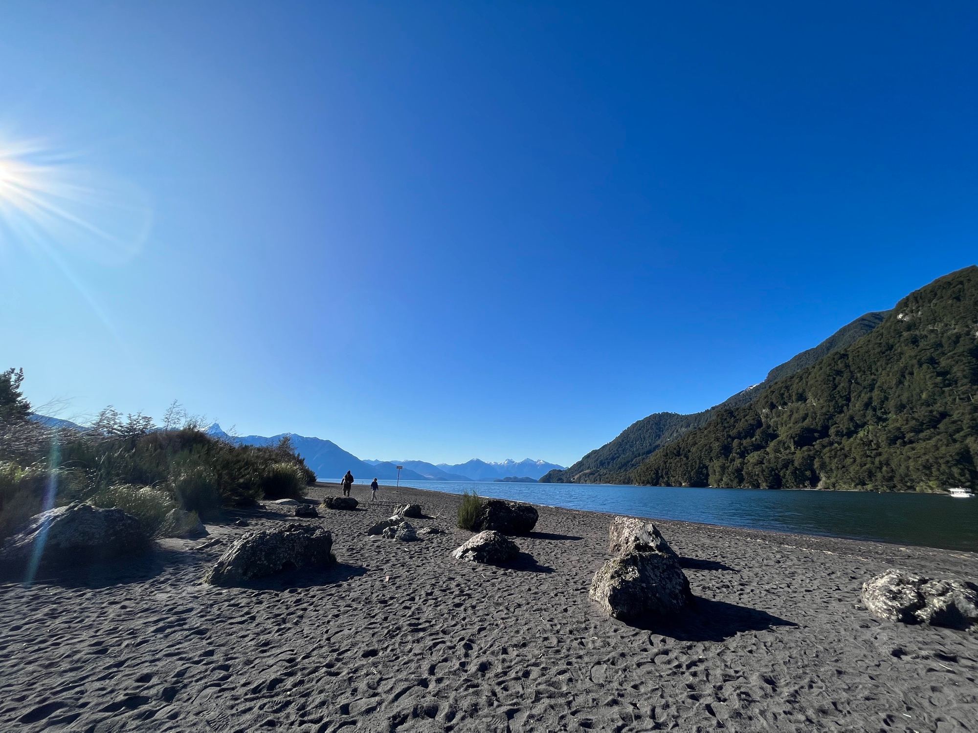 A beach of volcanic stones on the shore of Lake Todos los Santos, with forested hills