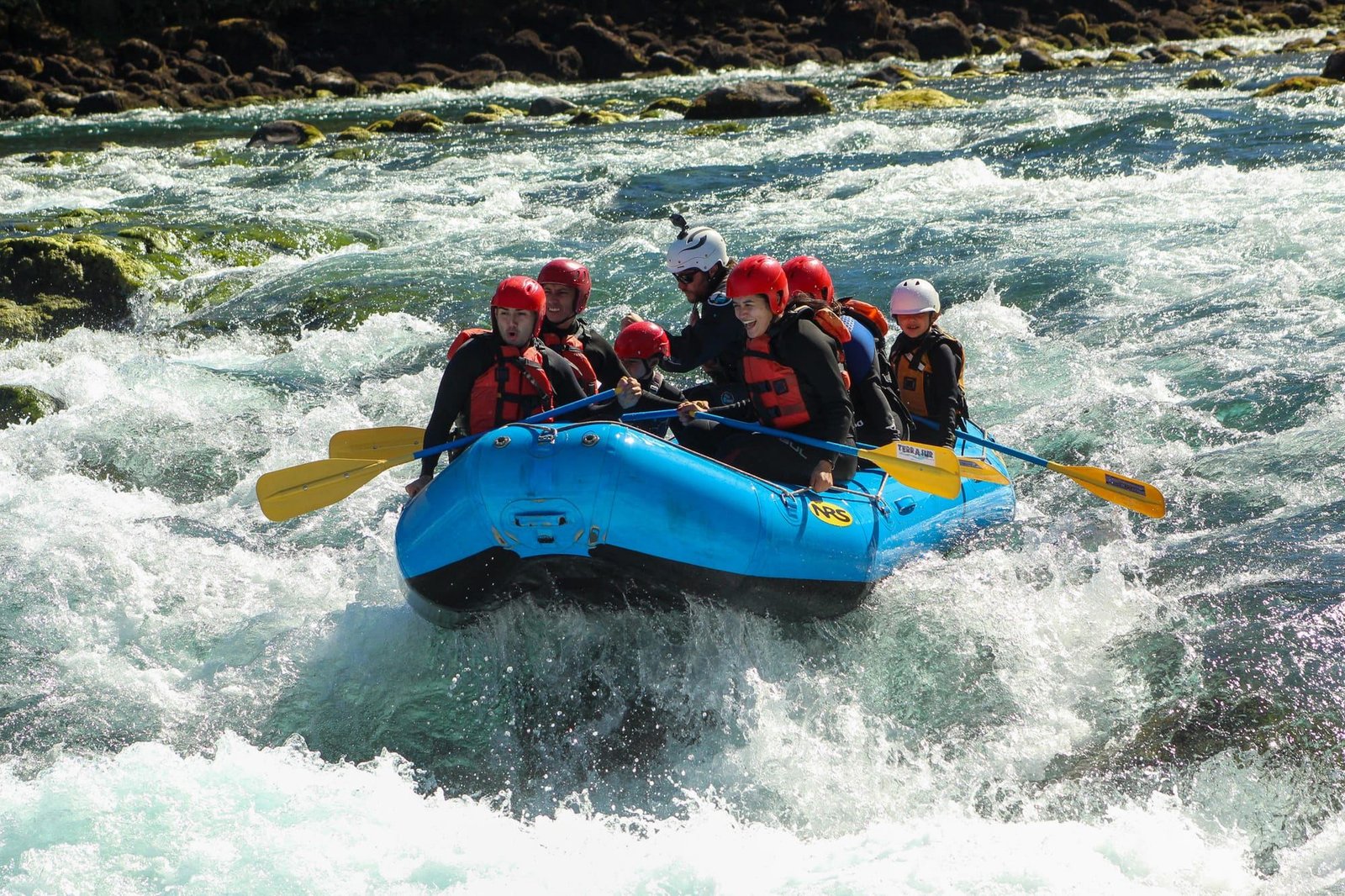A group in red helmets paddles a raft through a class III rapid