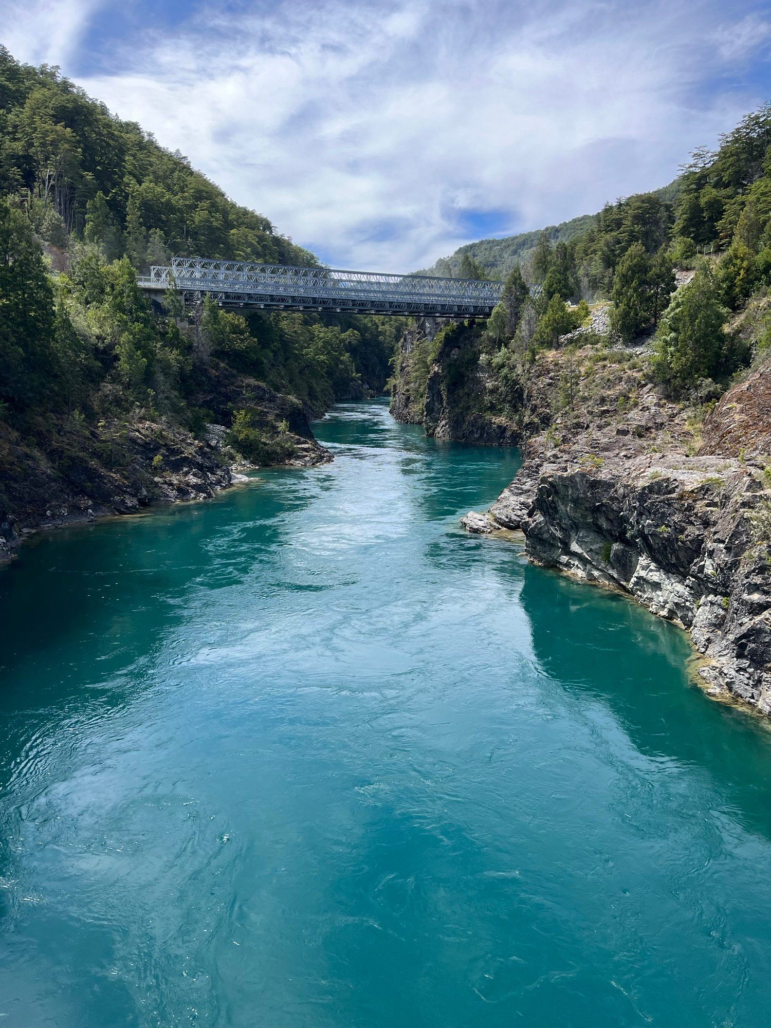 The turquoise Puelo River between rock walls and forest, with a bridge behind