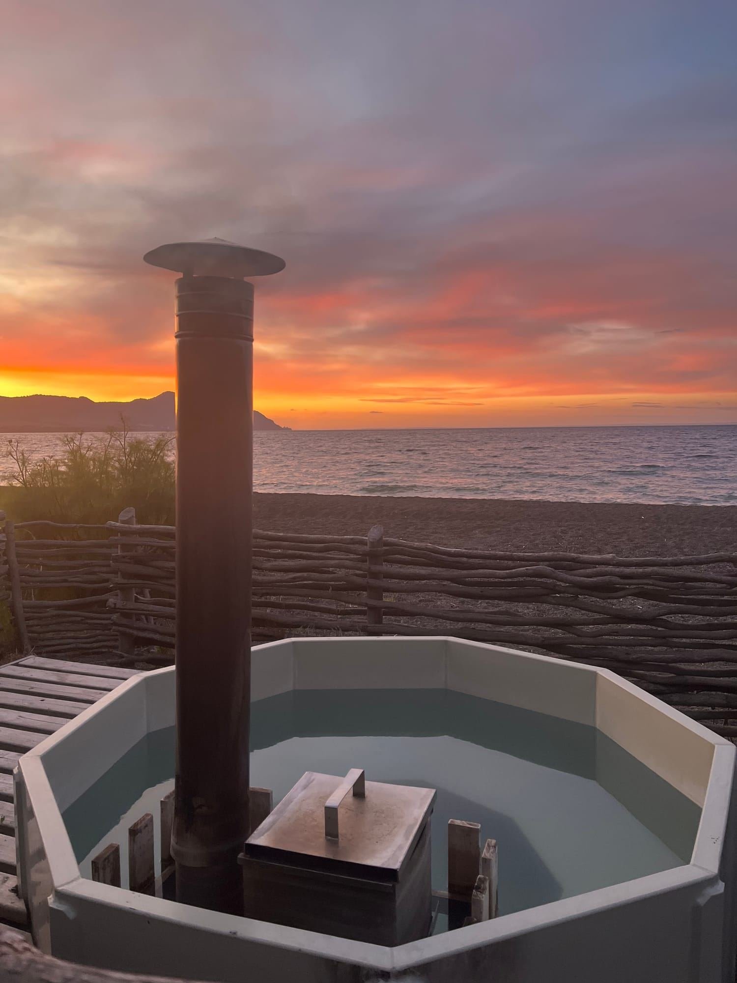 A wood-fired hot tub on the beach at sunset, facing Lake Llanquihue