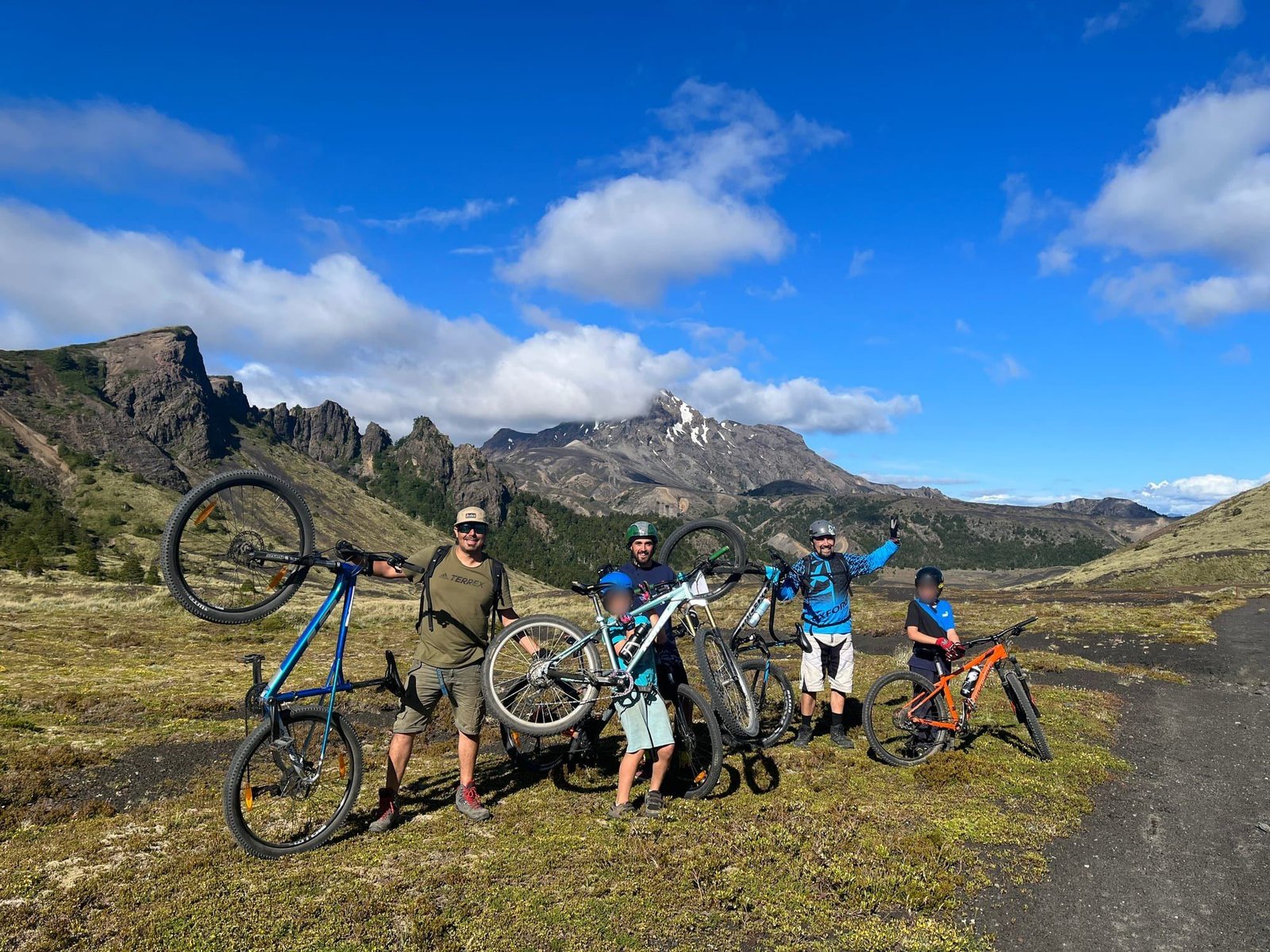 A group lifts their mountain bikes in a valley with rocky peaks