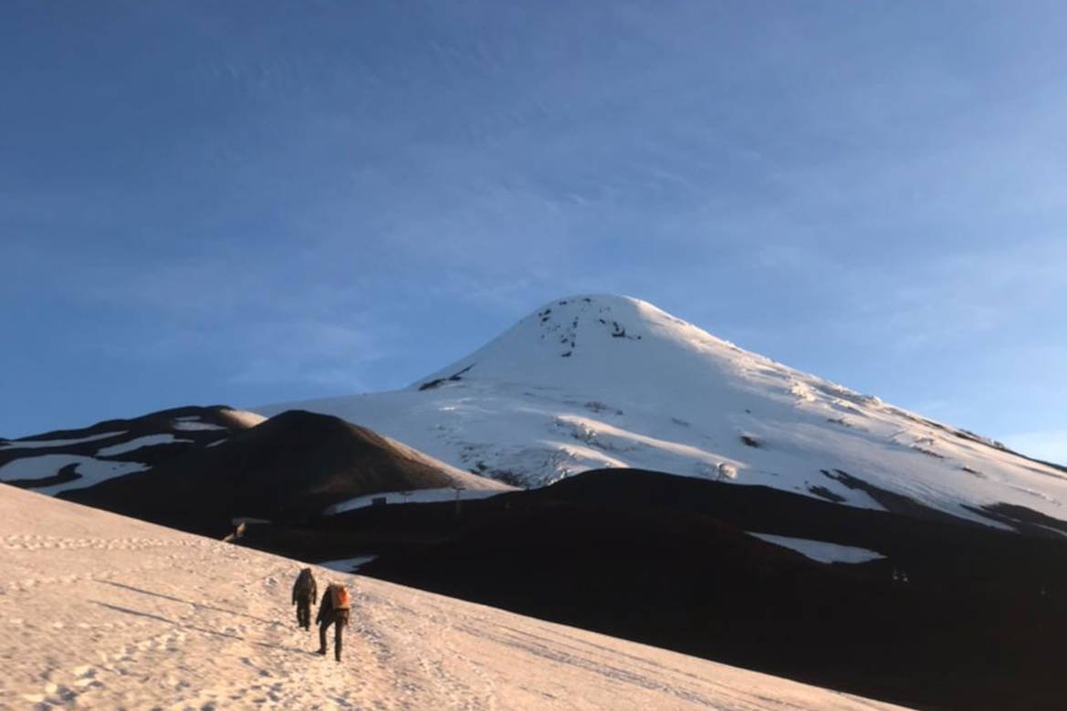 Two people walking across the snow toward the cone of Osorno Volcano