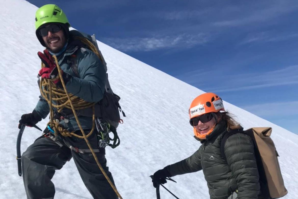 Guide with a rope and ice axe next to a climber in a helmet on the snowy slope